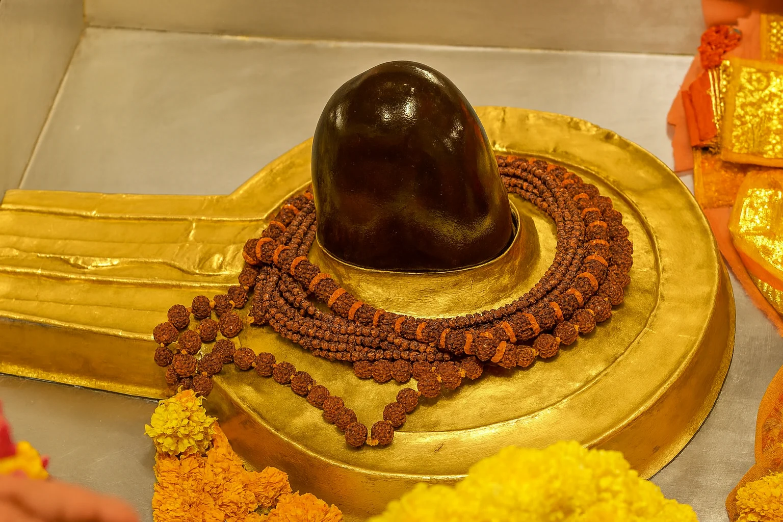 Sacred Shiva Lingam with Rudraksha and Golden Yoni A Shiva Lingam placed on a golden Yoni platform, adorned with Rudraksha beads and surrounded by marigold flowers.