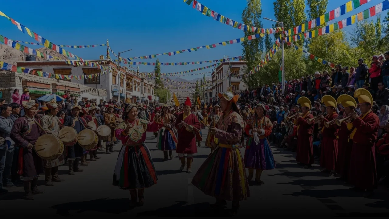 Rhythms of the High Himalayas Performers in colorful traditional Tibetan-style clothing dancing in a sunlit street decorated with Buddhist flags and surrounded by people.